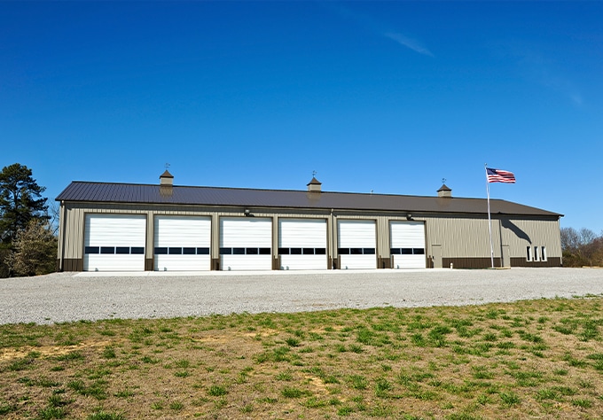 Metal buildings and roofing supplier in Baker, LA Walker Metals. Image of new brown commercial metal building with large garage bay doors and side office with American Flag on pole.