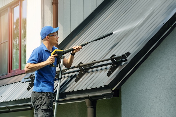man standing on ladder and demonstrating how to clean a metal roof